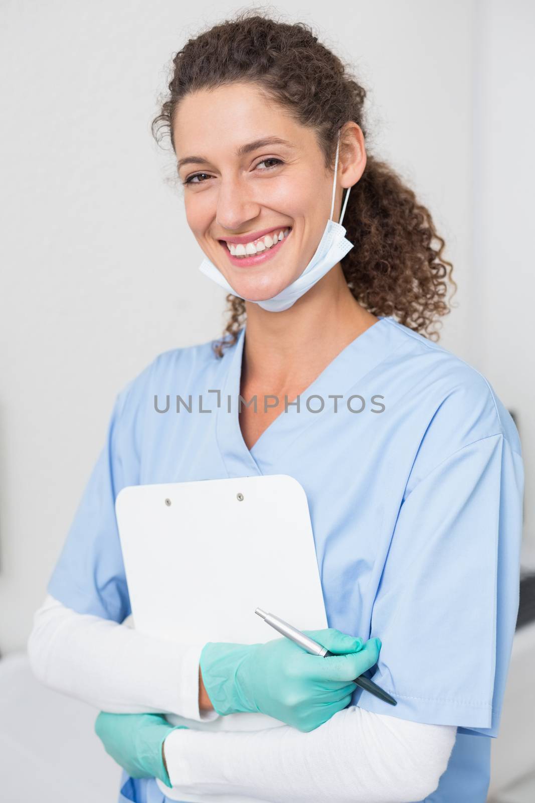 Dentist in blue scrubs smiling at camera holding clipboard by Wavebreakmedia