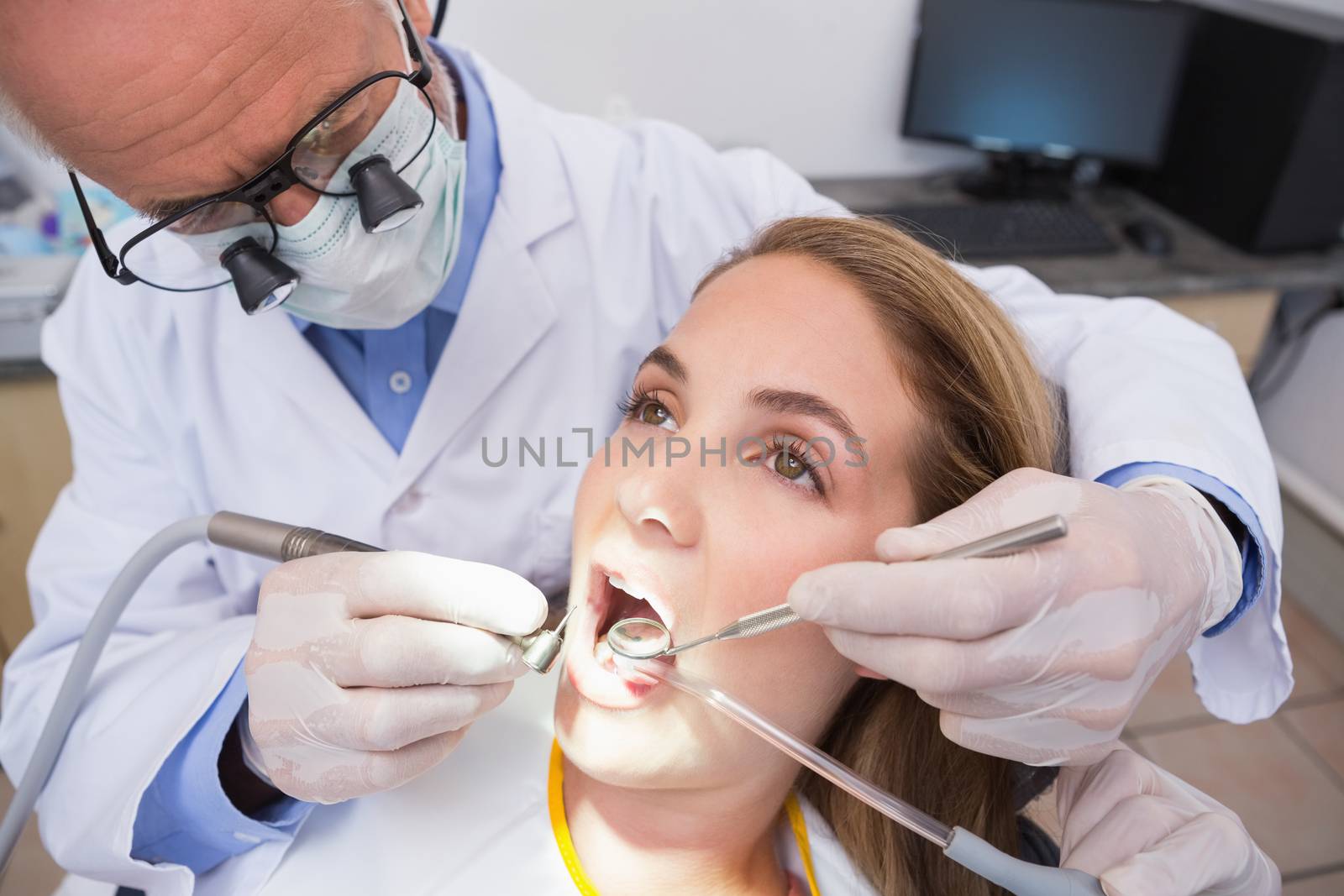 Dentist examining a patients teeth in the dentists chair with assistant at the dental clinic