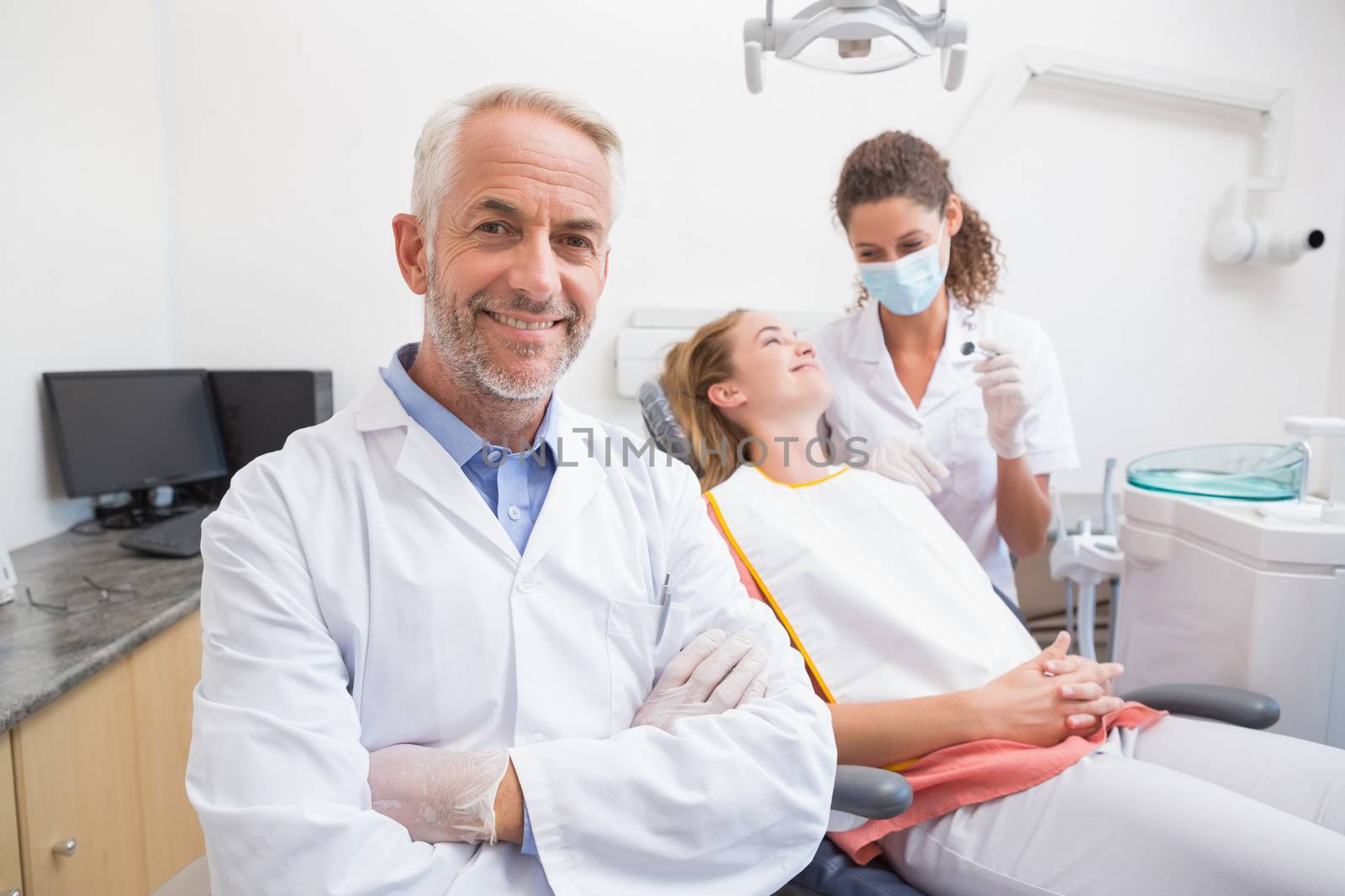 Dentist smiling at camera with assistant and patient behind by Wavebreakmedia