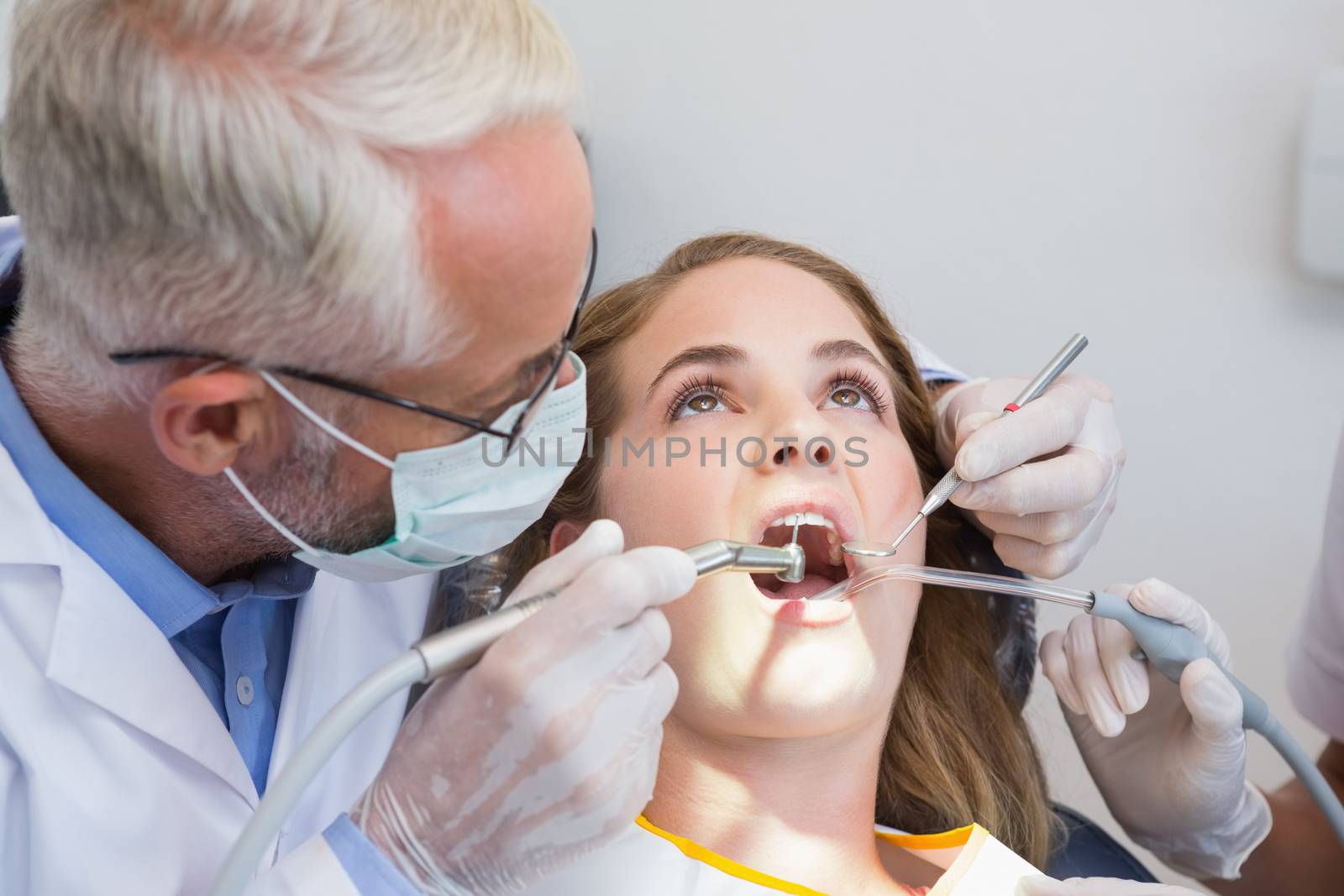 Dentist examining a patients teeth in the dentists chair with assistant by Wavebreakmedia