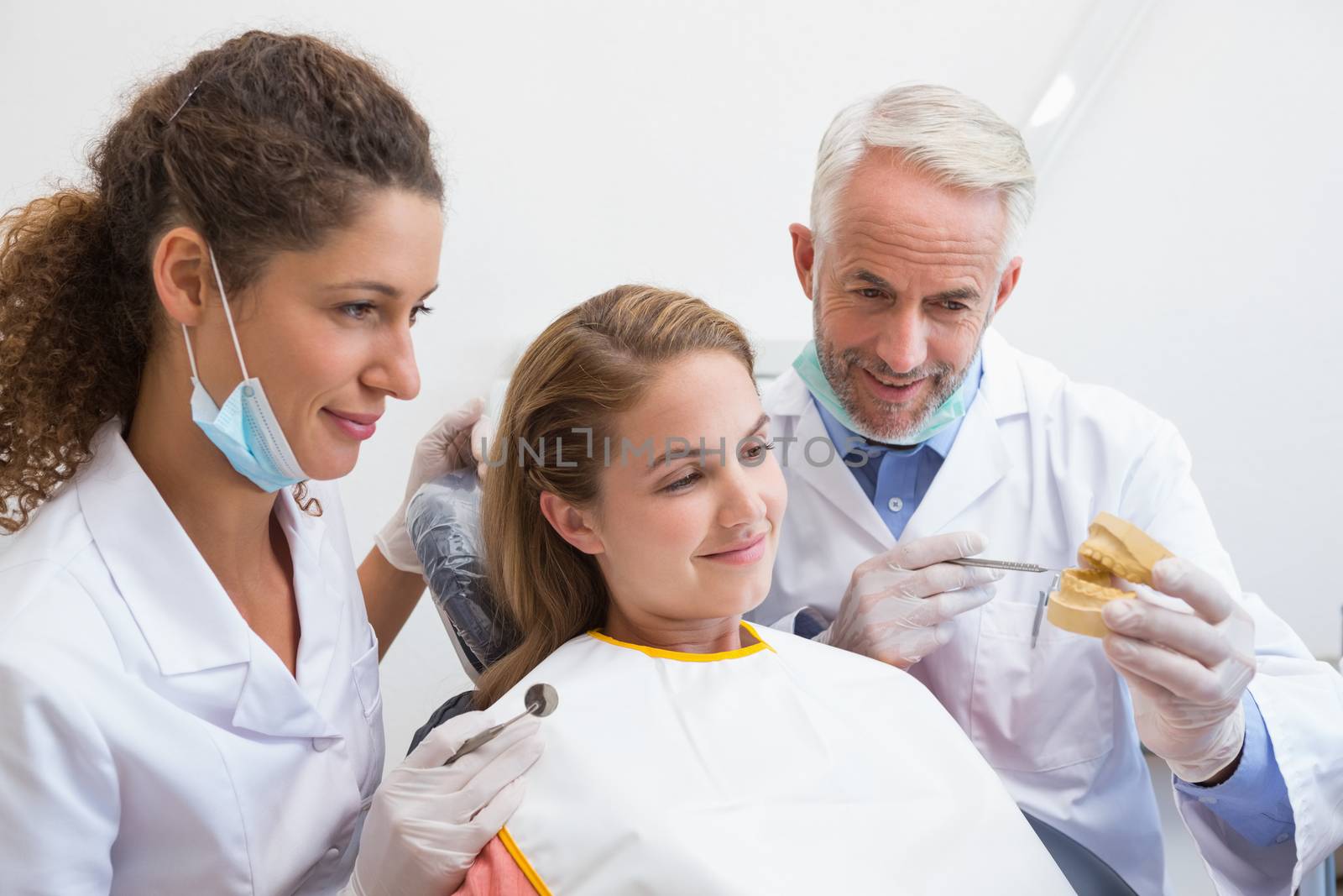 Dentist examining a patients teeth in the dentists chair with assistant at the dental clinic