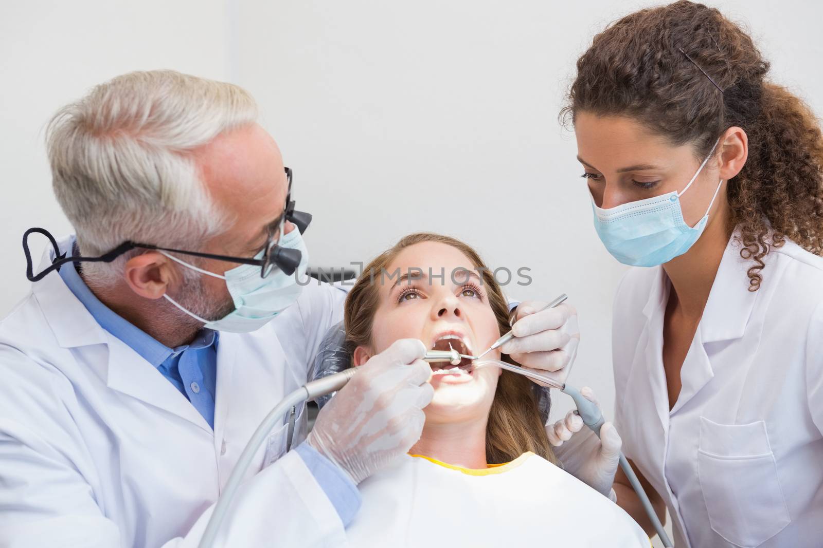 Dentist examining a patients teeth in the dentists chair with assistant at the dental clinic