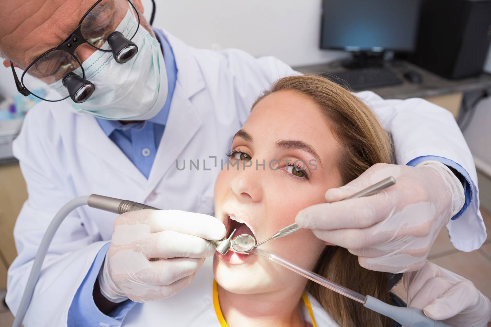 Dentist examining a patients teeth in the dentists chair with assistant at the dental clinic