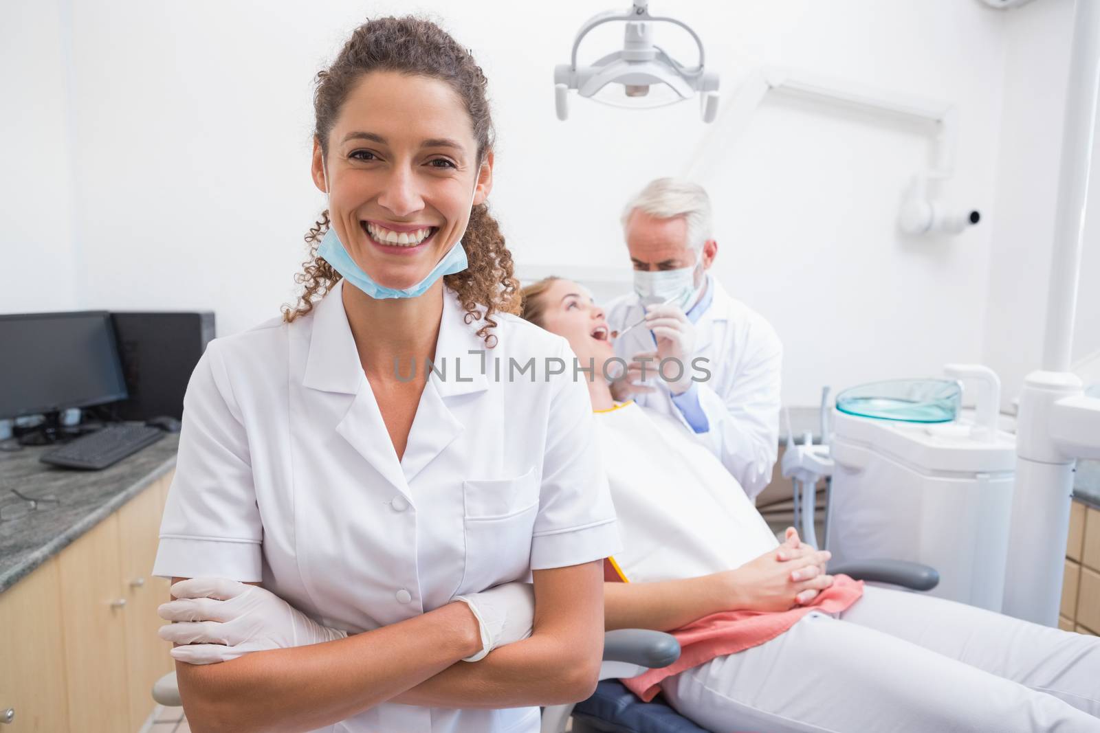 Dental assistant smiling at camera with dentist and patient behind by Wavebreakmedia