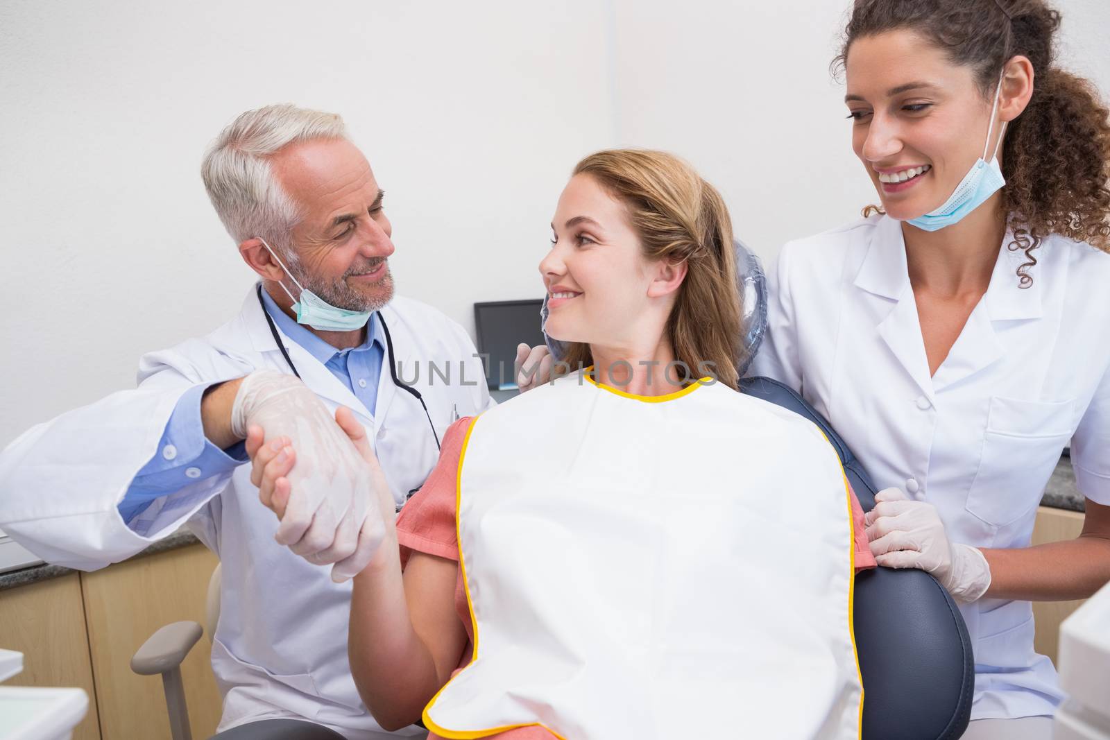 Dentist shaking hands with his patient in the chair beside assistant by Wavebreakmedia