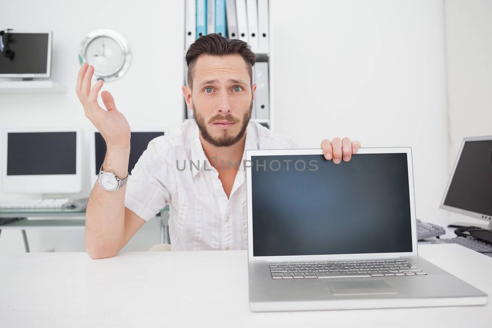 Confused computer engineer looking at camera with laptop by Wavebreakmedia