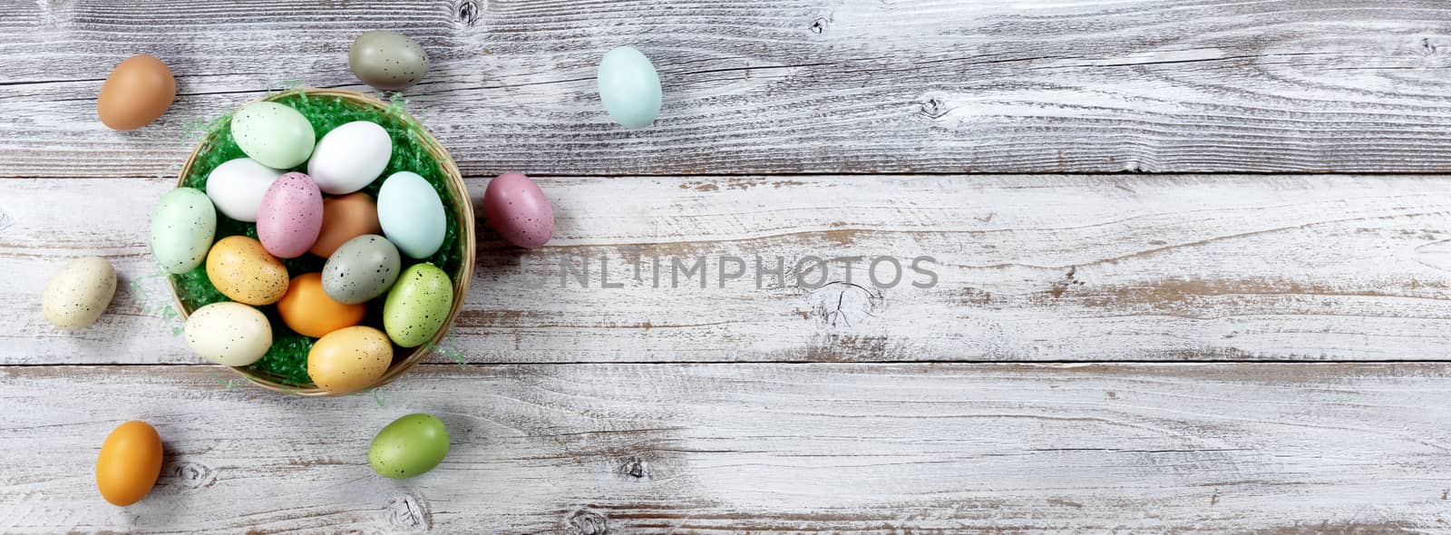Happy Easter holiday with basket filled of colorful eggs on white rustic wood. Overhead view with plenty of copy space 