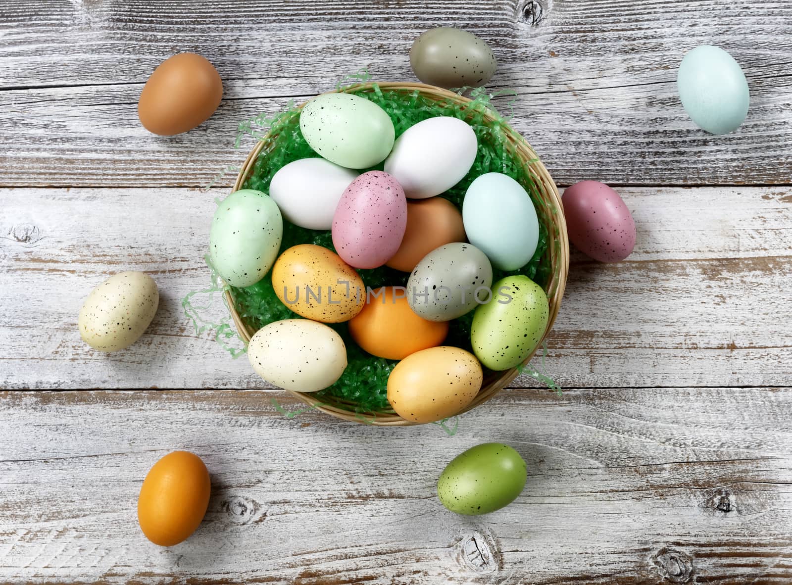 Happy Easter concept with basket filled of colorful eggs on white rustic wood. Overhead view layout 