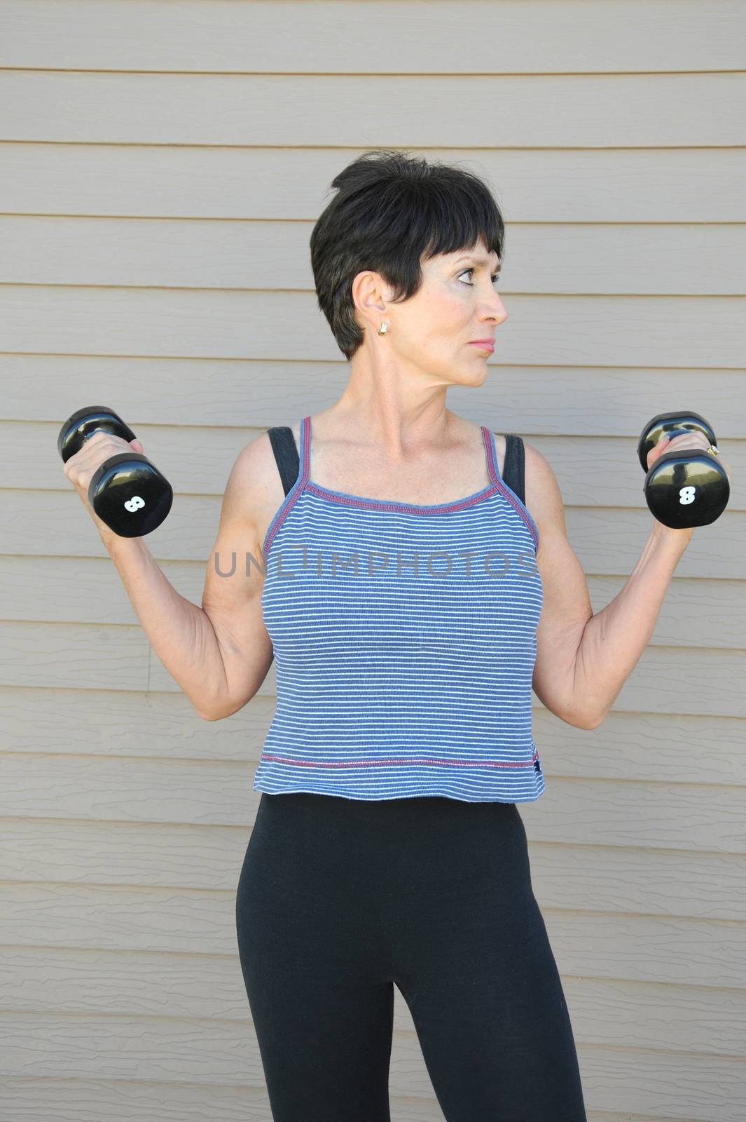 Mature female beauty working out with hand weights outside.
