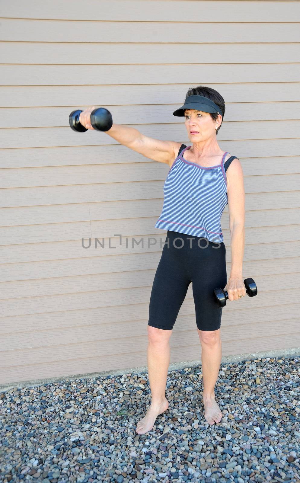 Mature female beauty working out with hand weights outside.