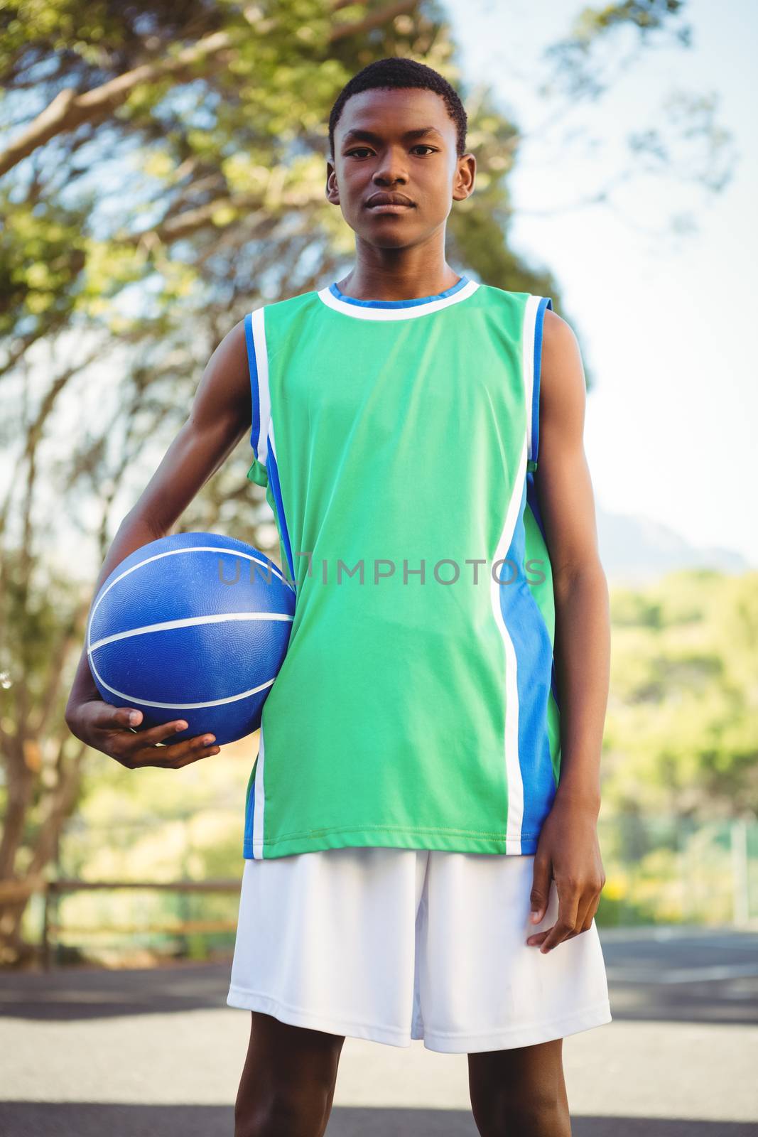 Portrait of serious man with basketball standing outdoors