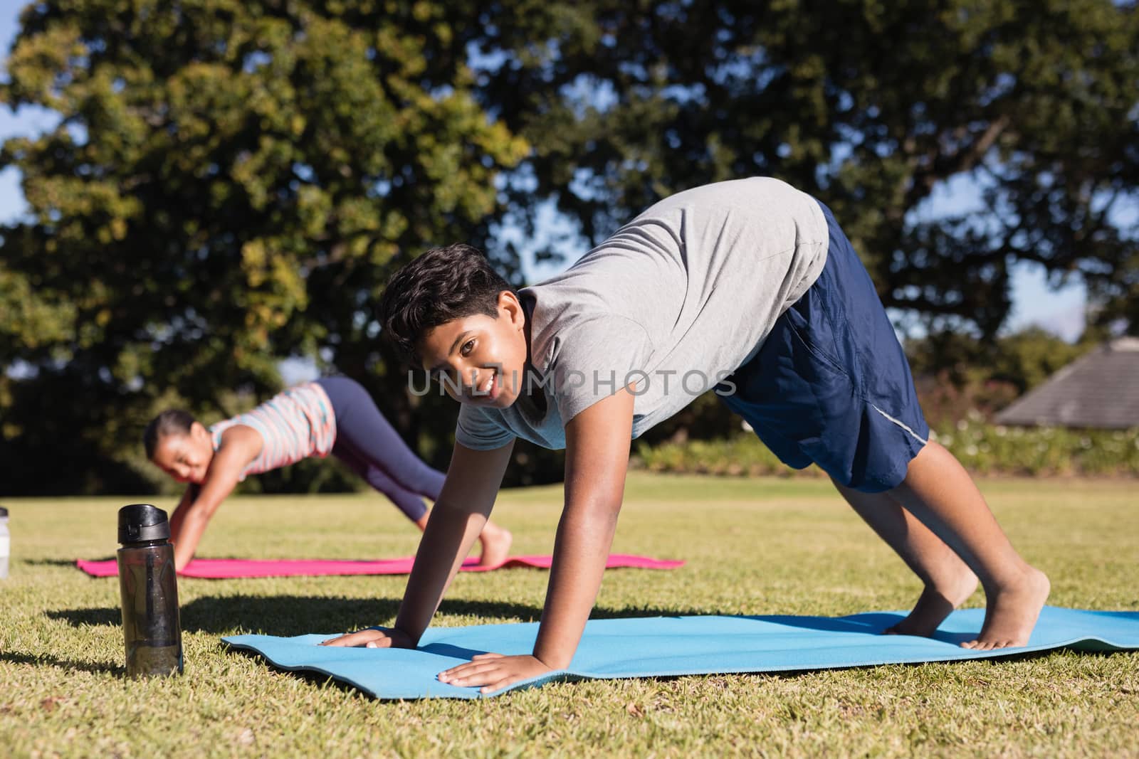 Portrait of happy boy practicing yoga on mat with female friend at park