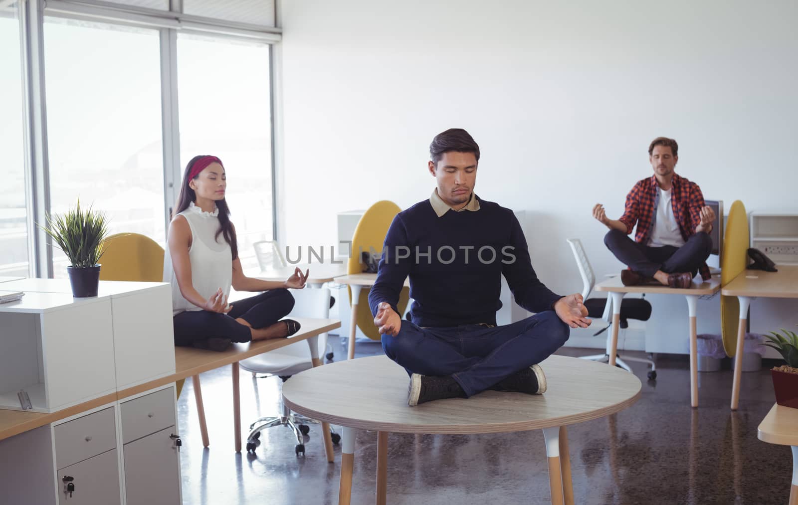 Business colleagues practicing yoga while sitting on desk at office