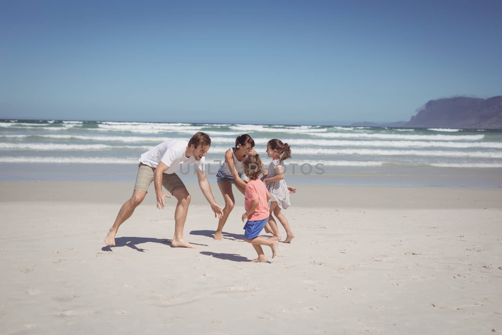 Happy family playing at beach against clear blue sky