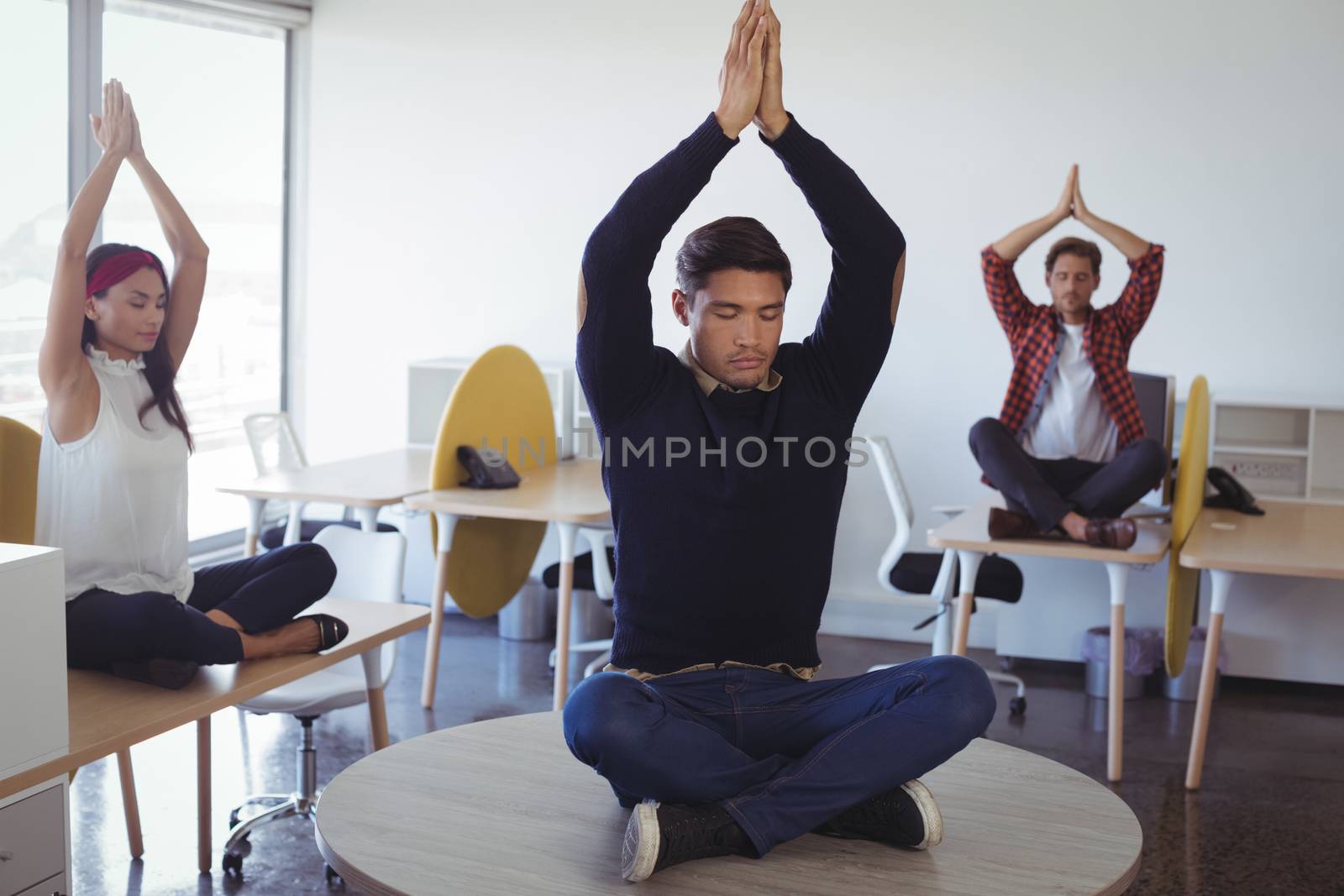 Business colleagues doing yoga while sitting on desk at office