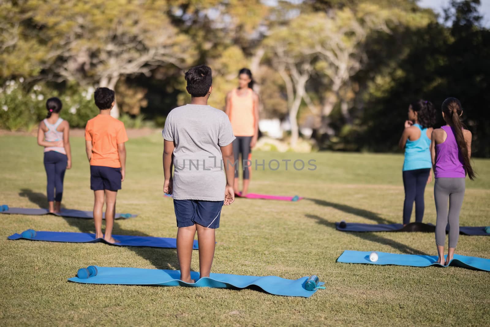 Children standing on exercise mat practicing yoga at park during summer camp
