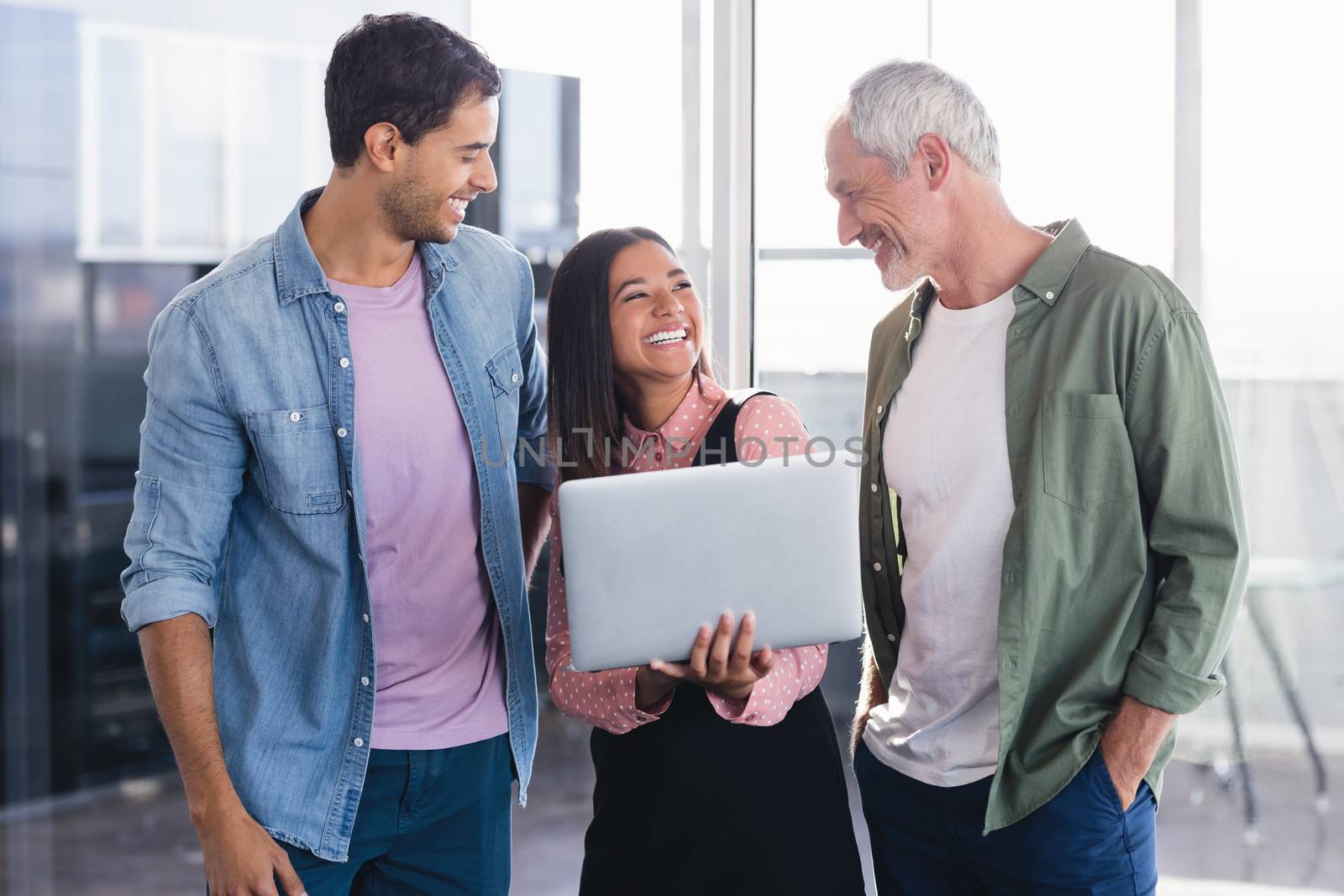 Cheerful business people with laptop standing in office