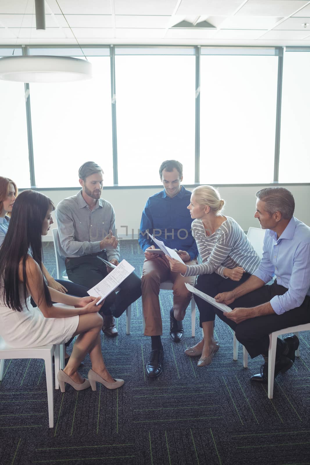 Business people discussing over documents while sitting on chairs at office