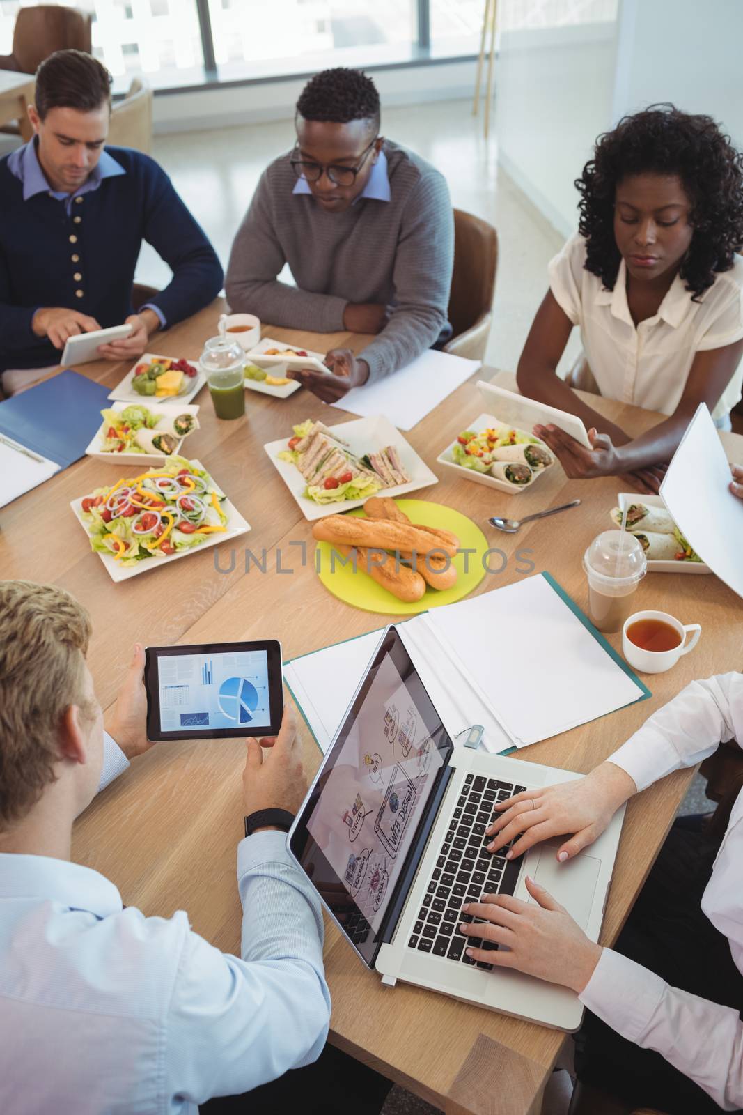 Business people using laptop and digital tablets around breakfast table by Wavebreakmedia