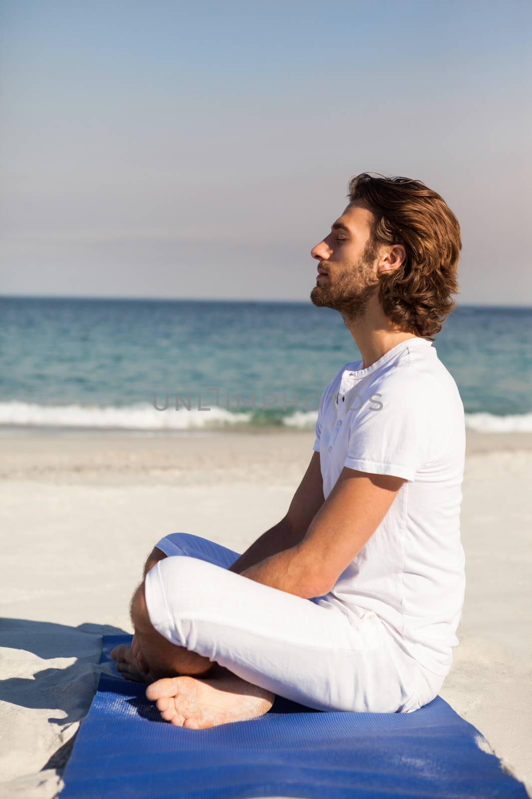 Man performing yoga at beach by Wavebreakmedia