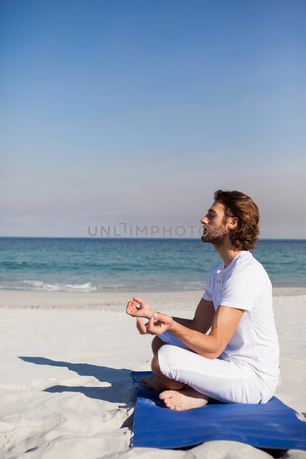 Man performing yoga at beach on a sunny day