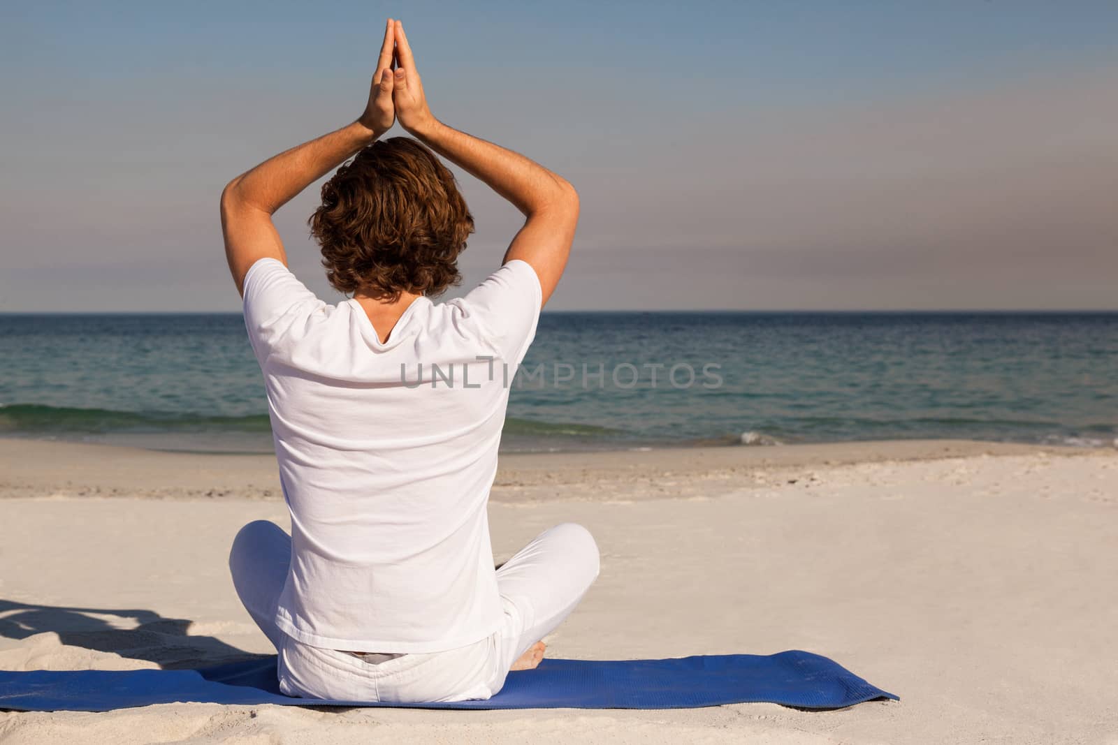 Rear view of man performing yoga at beach on sunny day