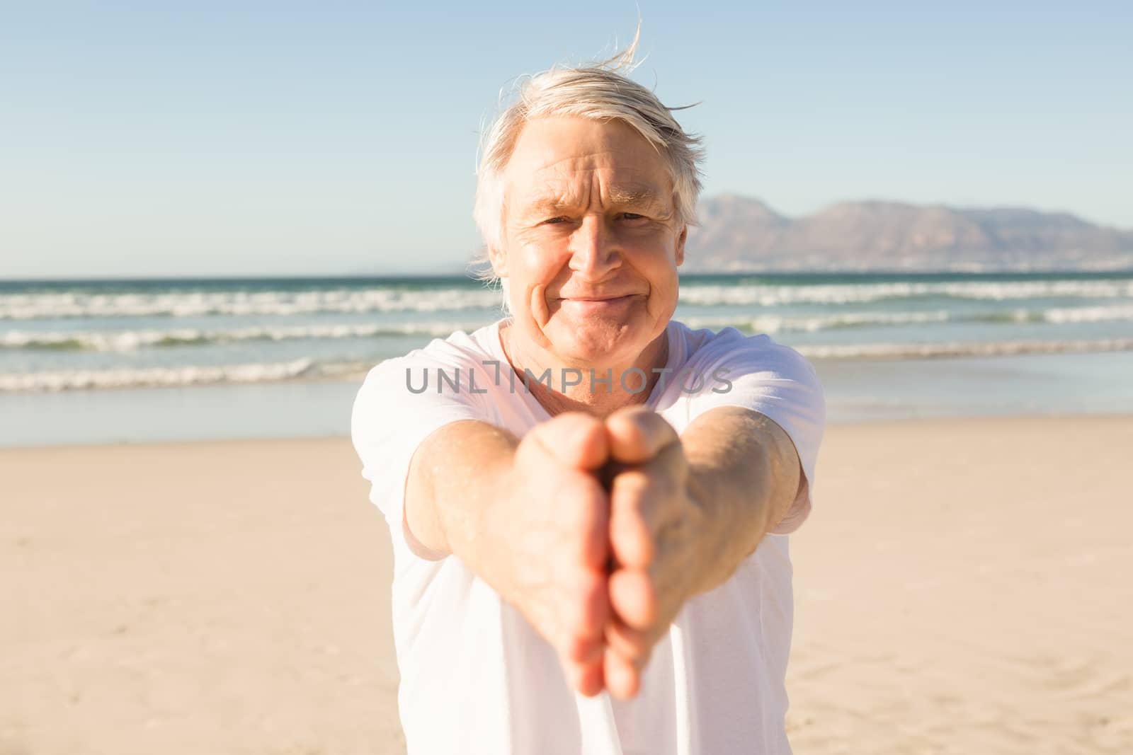 Portrait of senior man practicing yoga at beach on sunny day