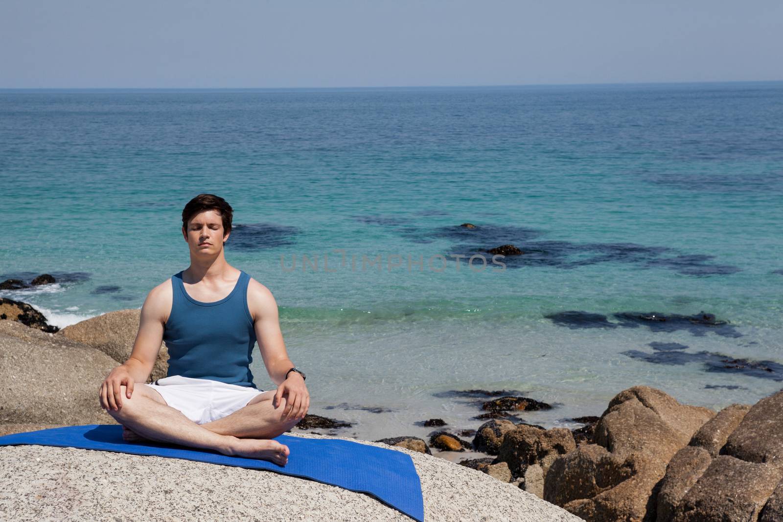 Man performing yoga on rock near the coast