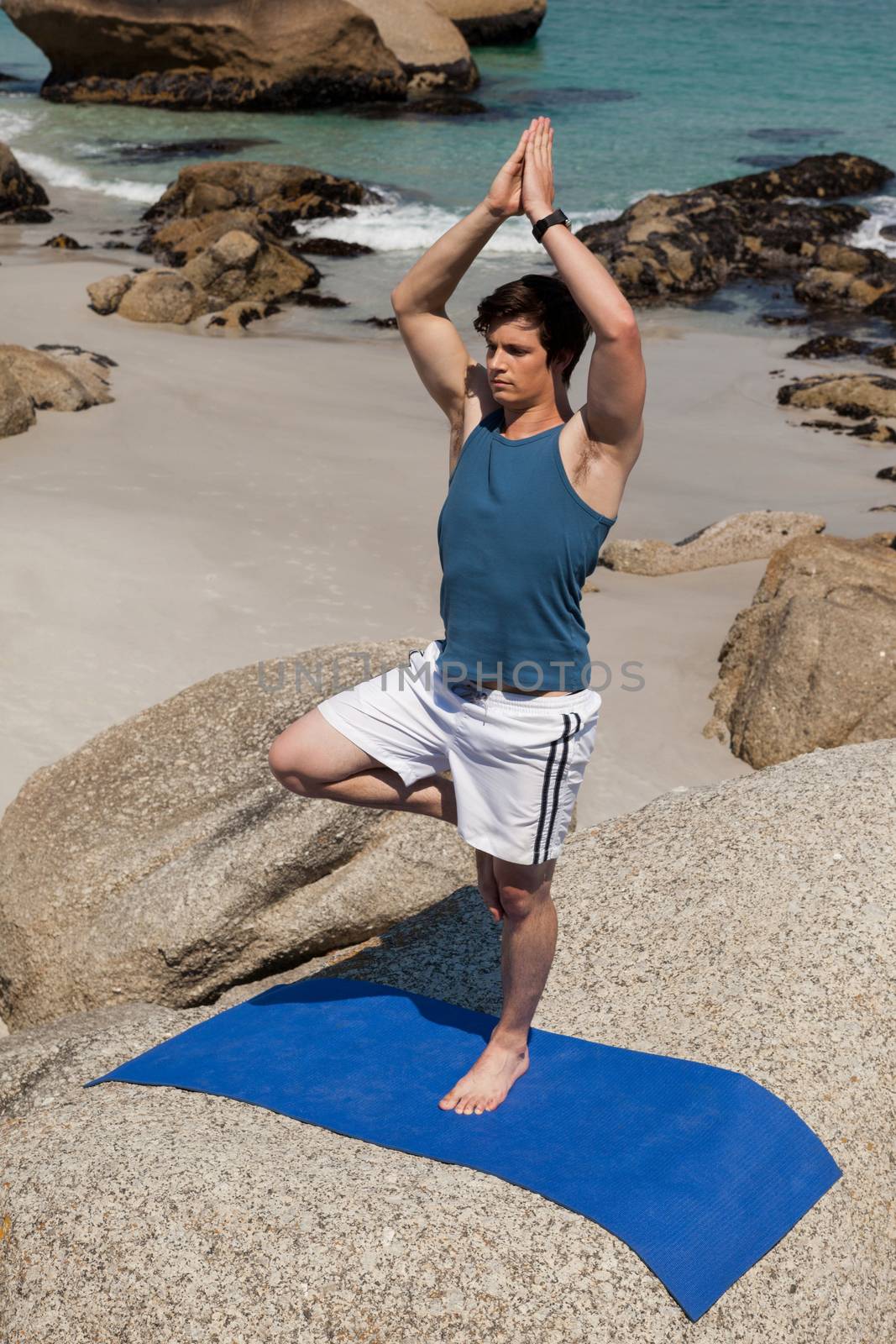 Man performing yoga on rock near the coast