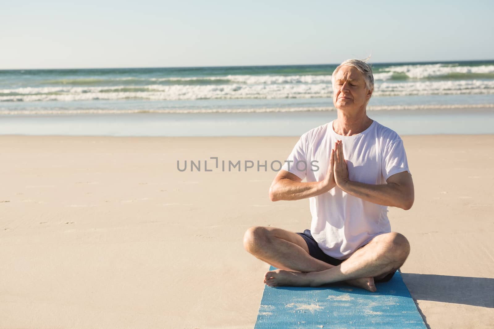 Senior man doing yoga while sitting at beach on sunny day