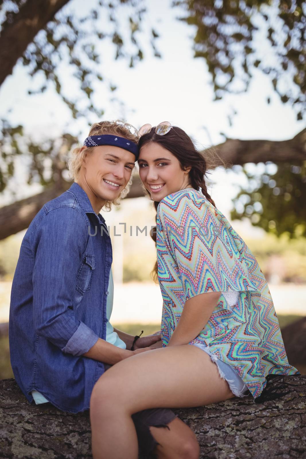 Side view portrait of smiling romantic couple sitting on tree trunk at forest