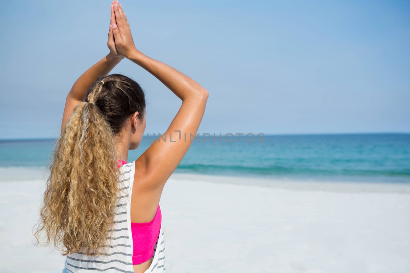 Woman practicing yoga at beach against clear blue sky