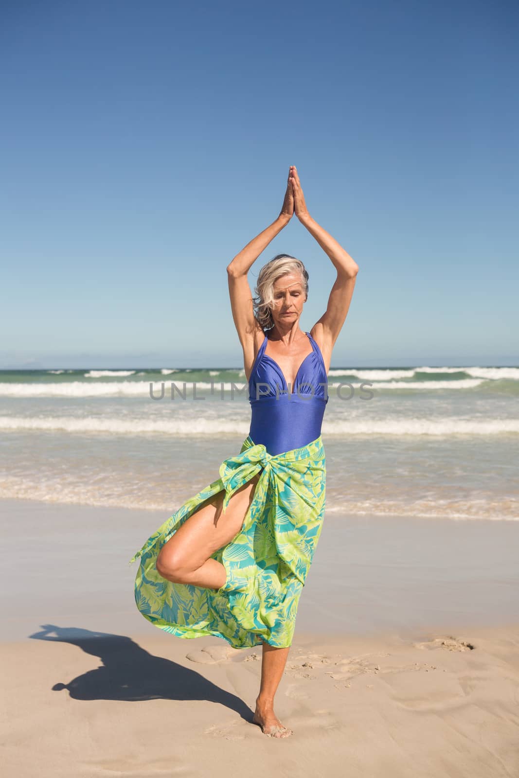 Senior woman practising yoga while standing against sea by Wavebreakmedia