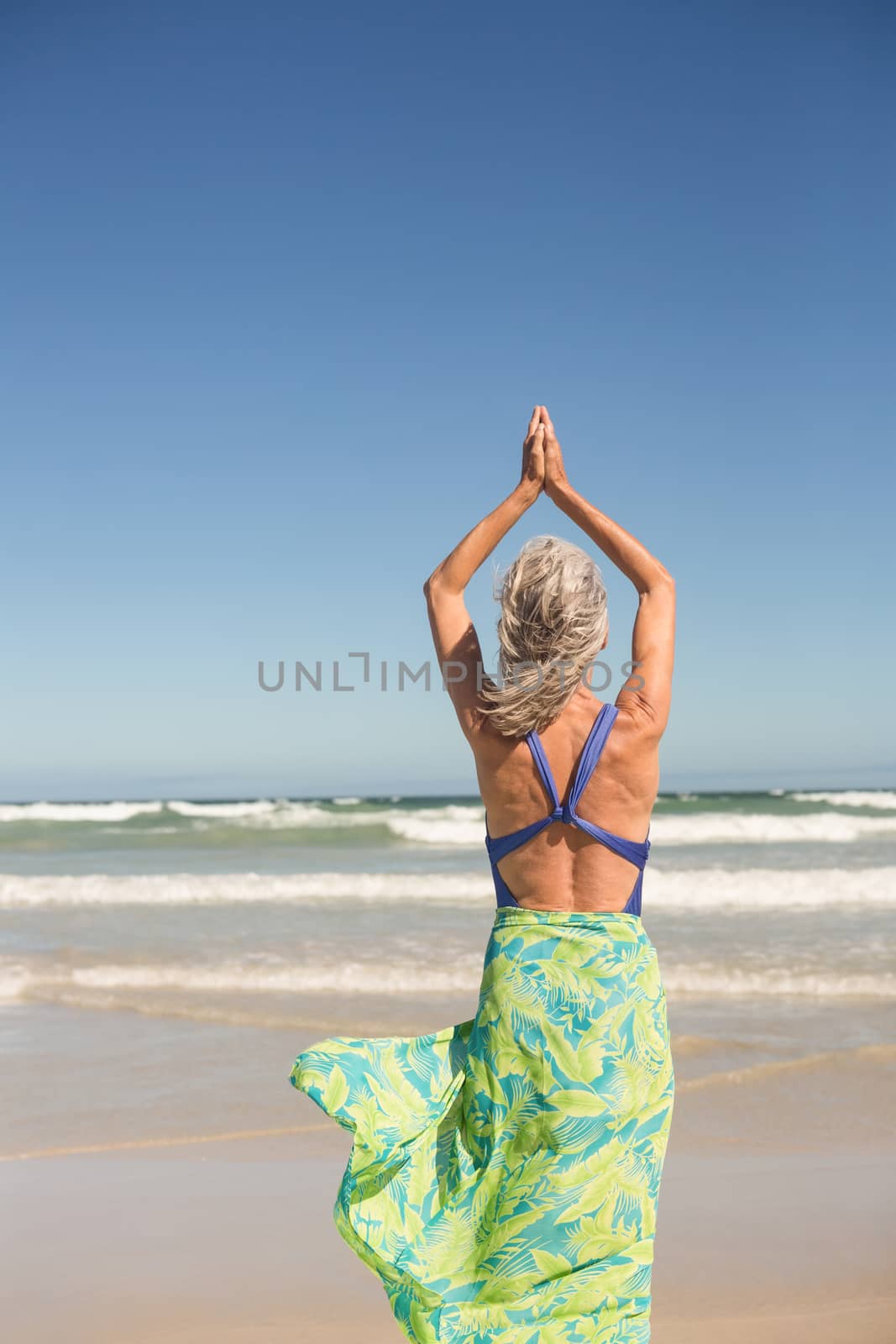 Rear view of woman practising yoga while standing against sea at beach