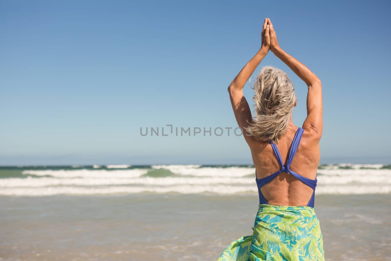 Woman practising yoga while standing at beach by Wavebreakmedia