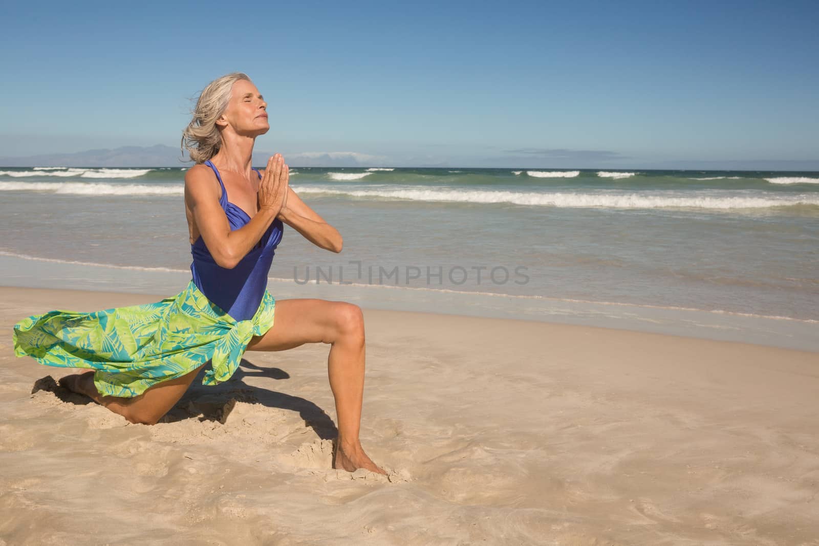 Senior woman practising yoga on sand at beach