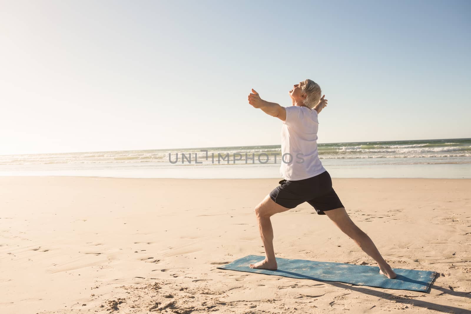 Active senior man practicing yoga at beach on sunny day