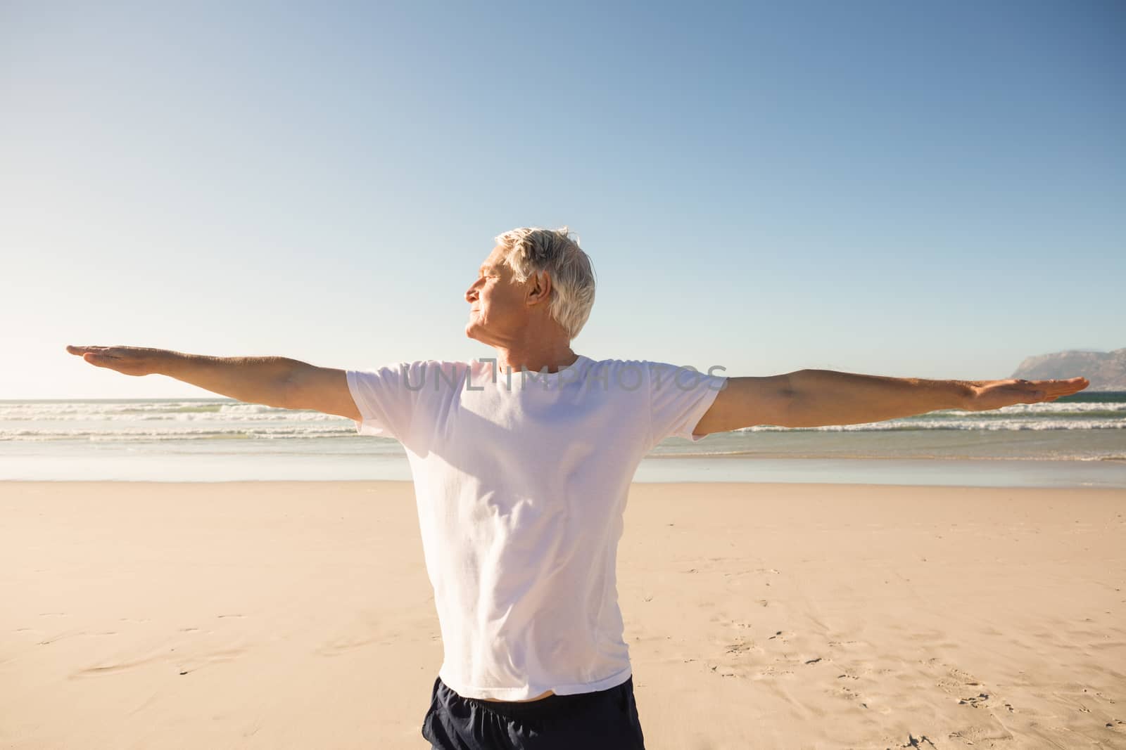 Senior man practicing yoga at beach on sunny day