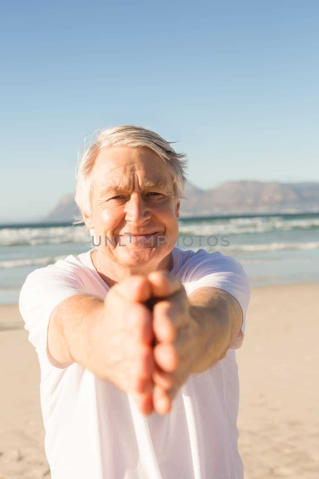 Portrait of active senior man practicing yoga at beach on sunny day
