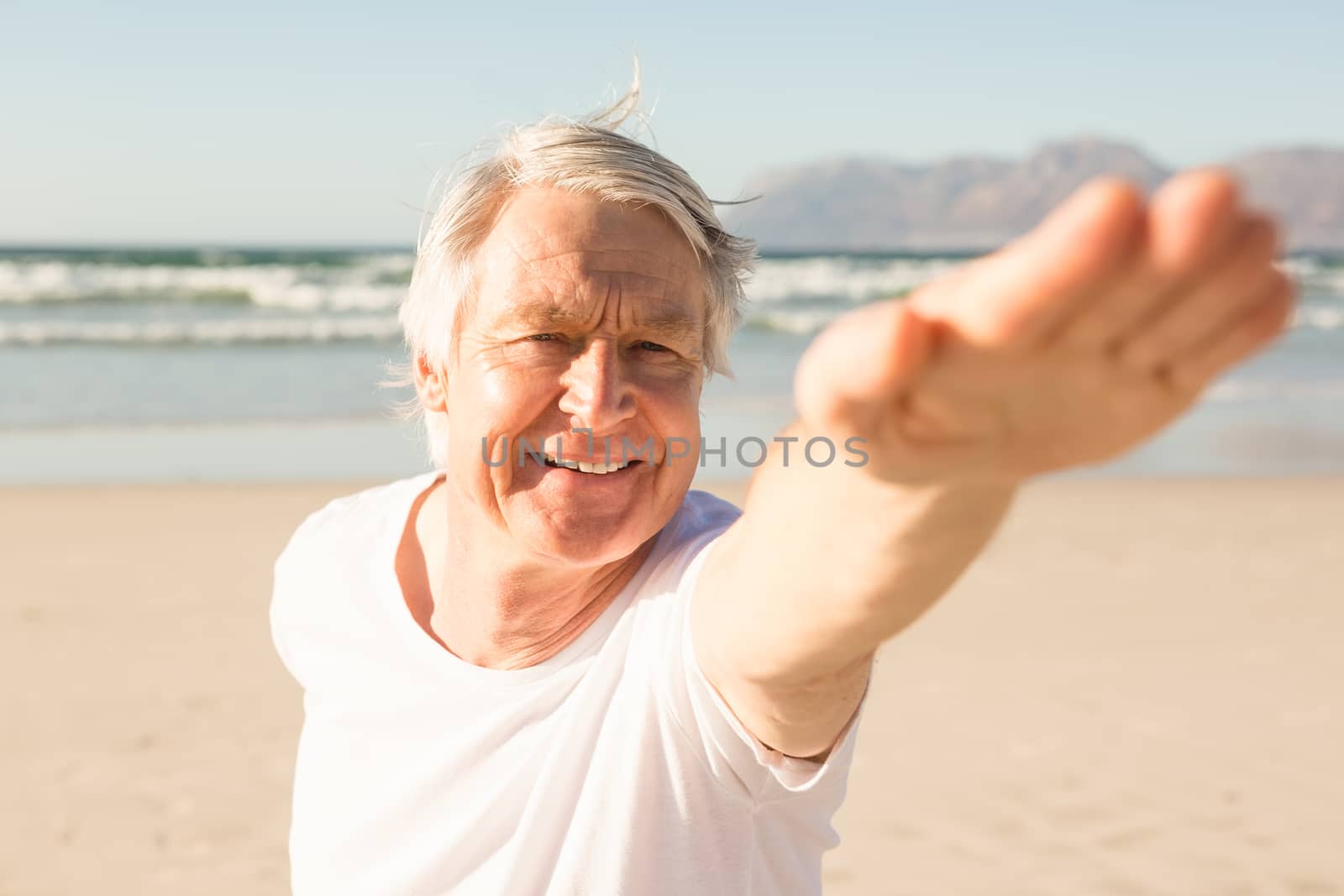 Happy senior man practicing yoga at beach on sunny day