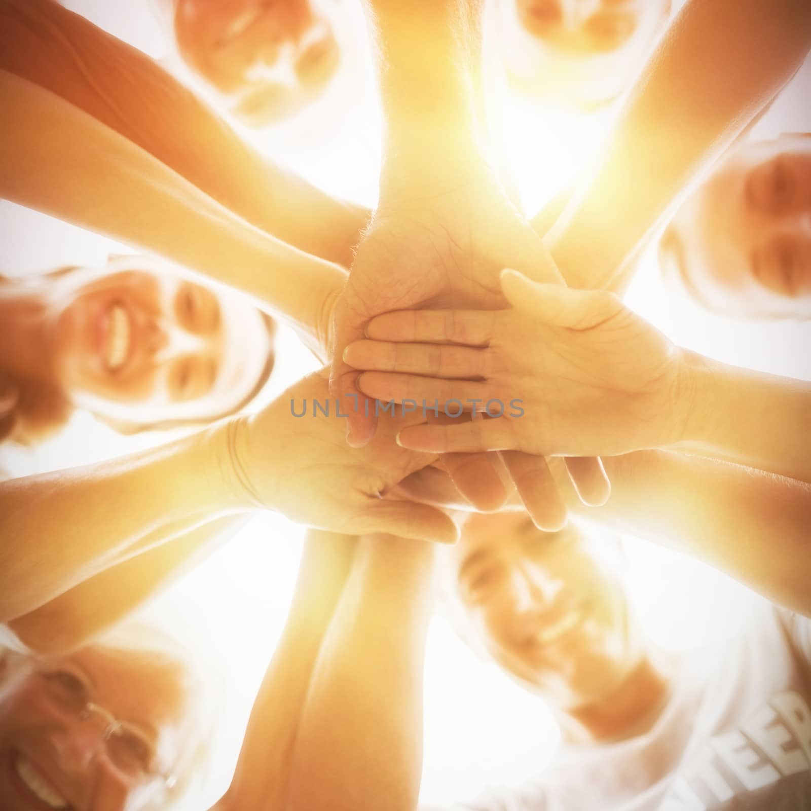 Happy volunteers putting their hands together against sky