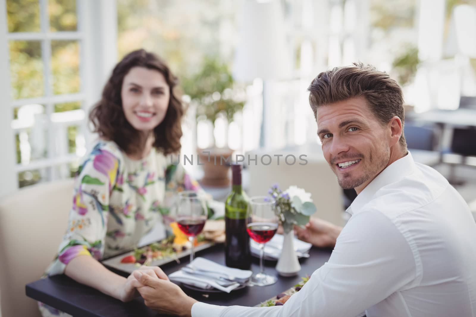 Portrait of romantic couple holding hands while having meal in restaurant