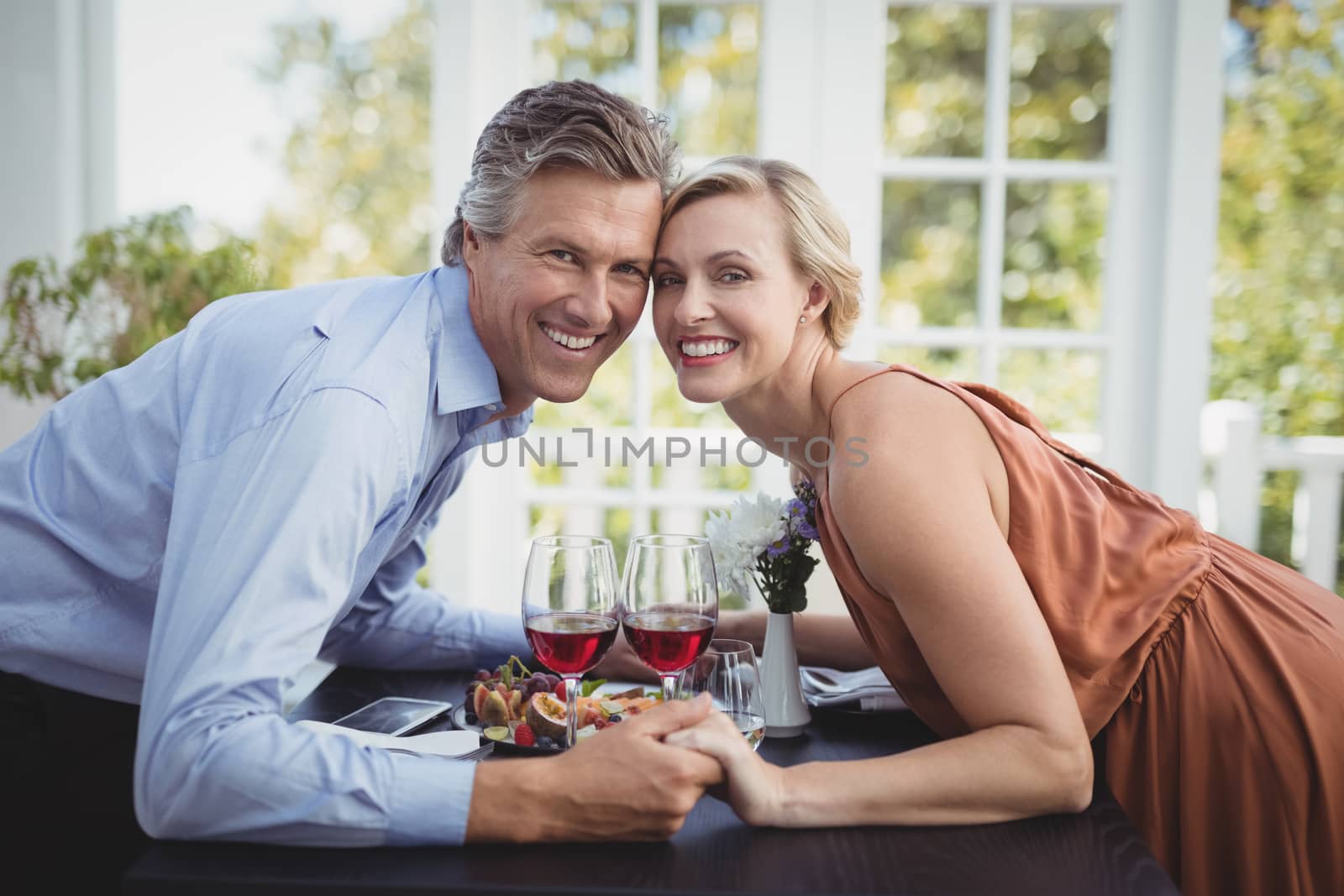 Portrait of romantic couple holding hands while having meal in restaurant