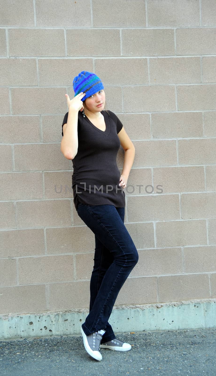 Female tomboy posing against a wall outside.