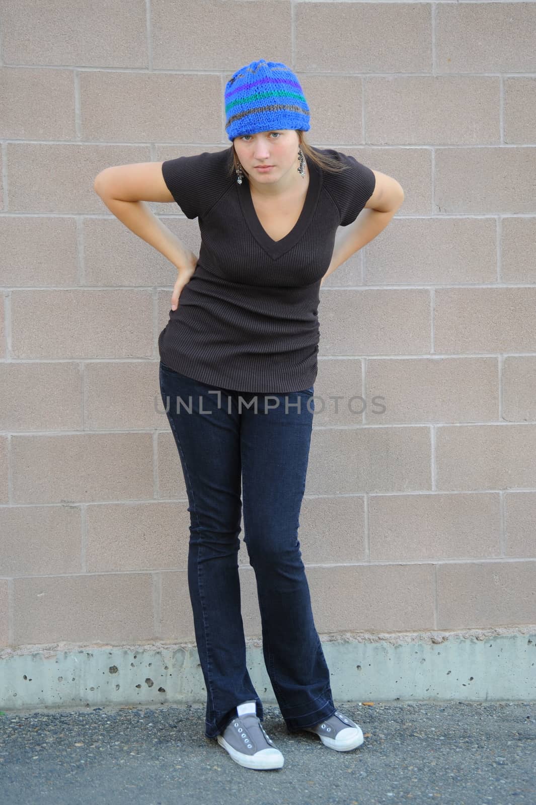 Female tomboy posing against a wall outside.