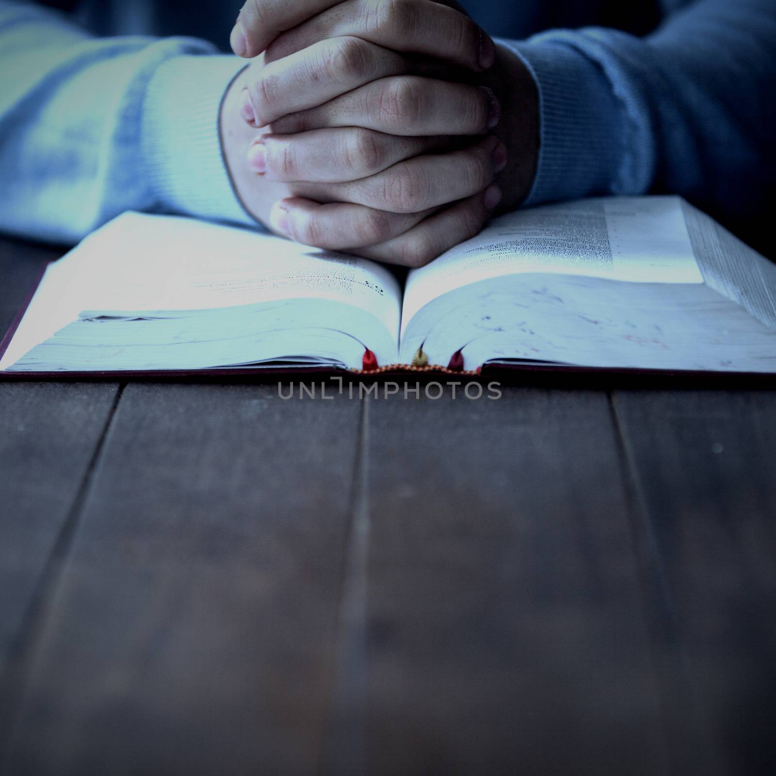 Mid section of man with bible praying at wooden desk