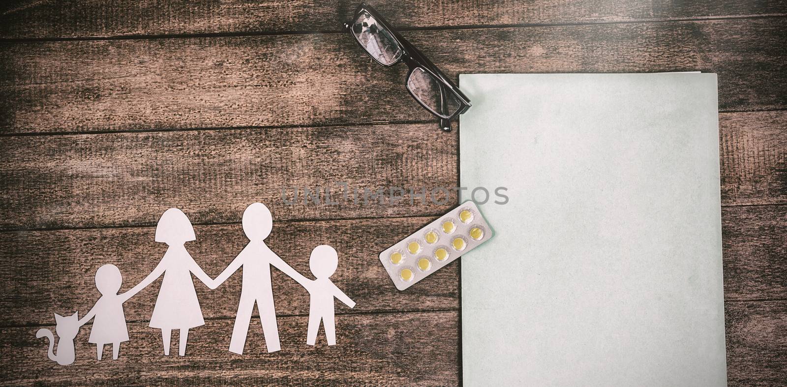 Overhead view of paper cut out family chain with medicine and file on table