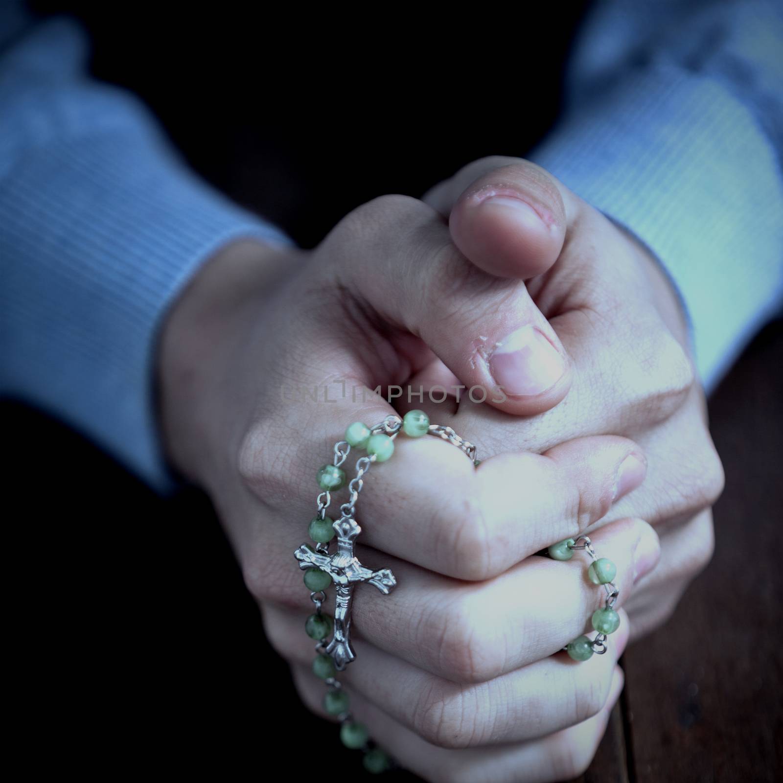 Praying hands of man with rosary on wooden desk