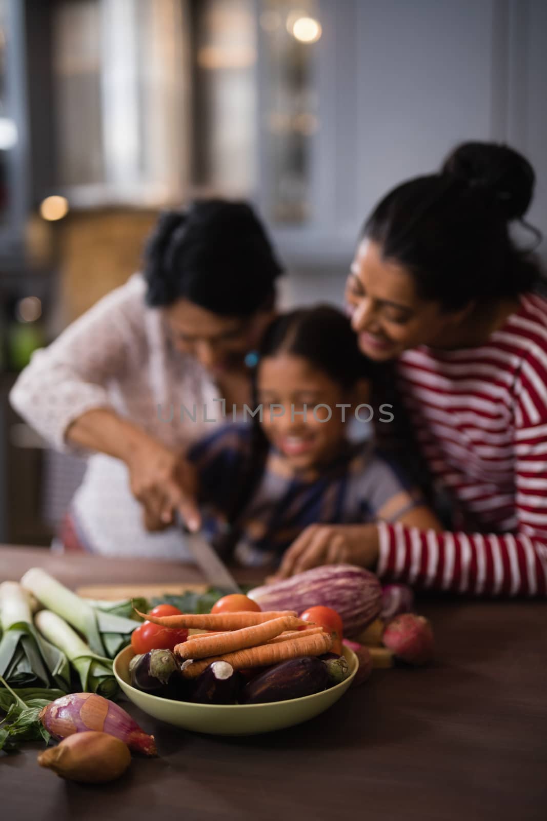 Vegetables on table against multi-generation family preparing food in kitchen by Wavebreakmedia