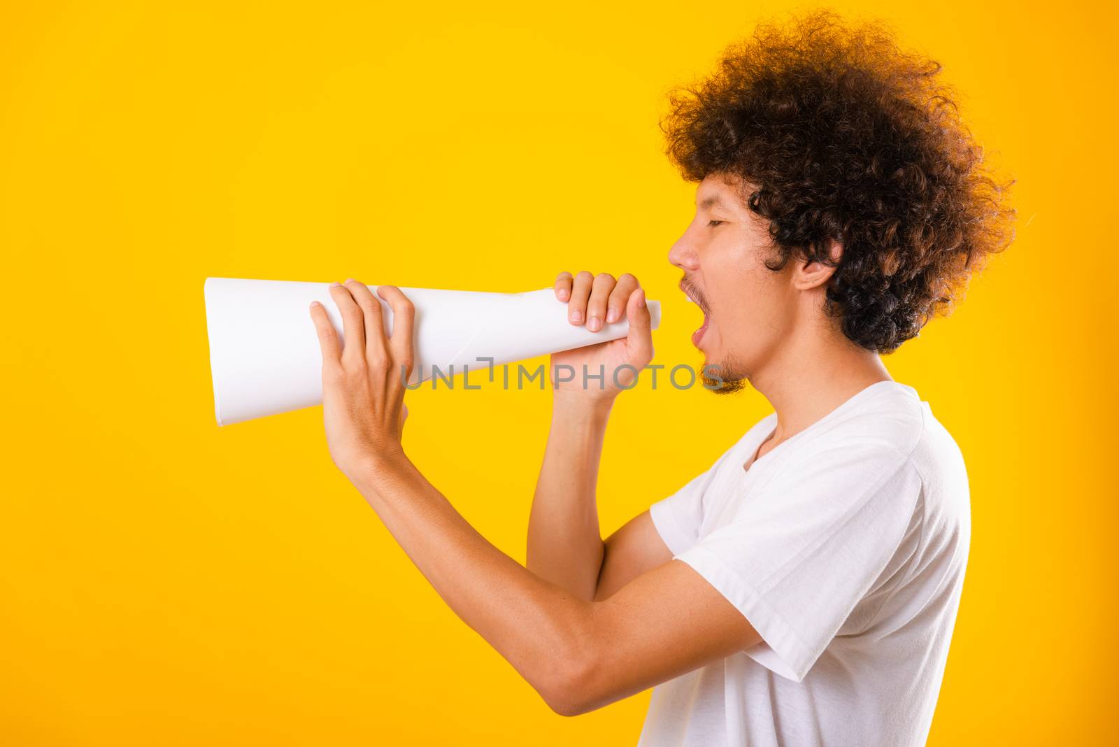 Asian handsome man with curly hair he announcing or spreading news using white speaker paper isolate on yellow background